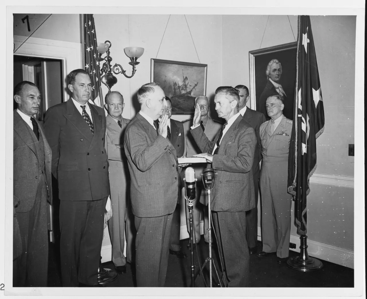 James Forrestal raises his right hand as Chief Justice Fred Vinson swears him in as the first Secretary of Defense, with military and civilian officials standing behind them, September 17, 1947.