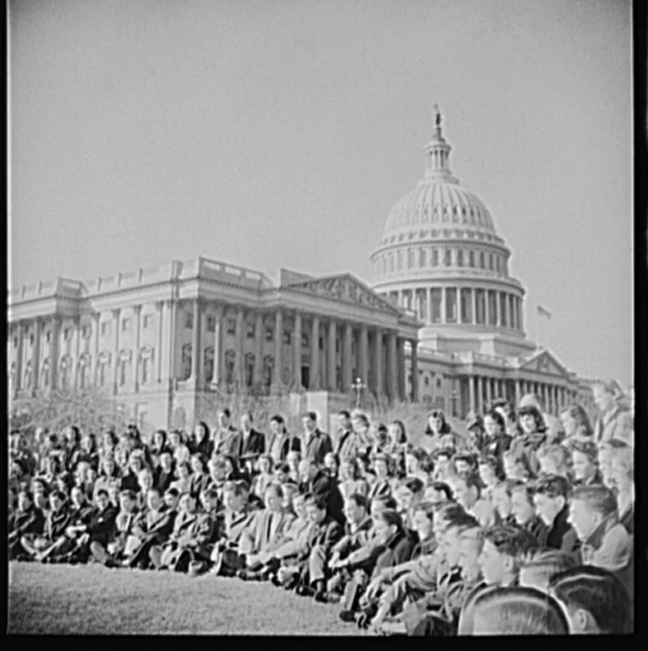 A large group of American high school students seated on the lawn in front of the United States Capitol during a 1942 civics study trip to Washington, with the Capitol dome behind them.