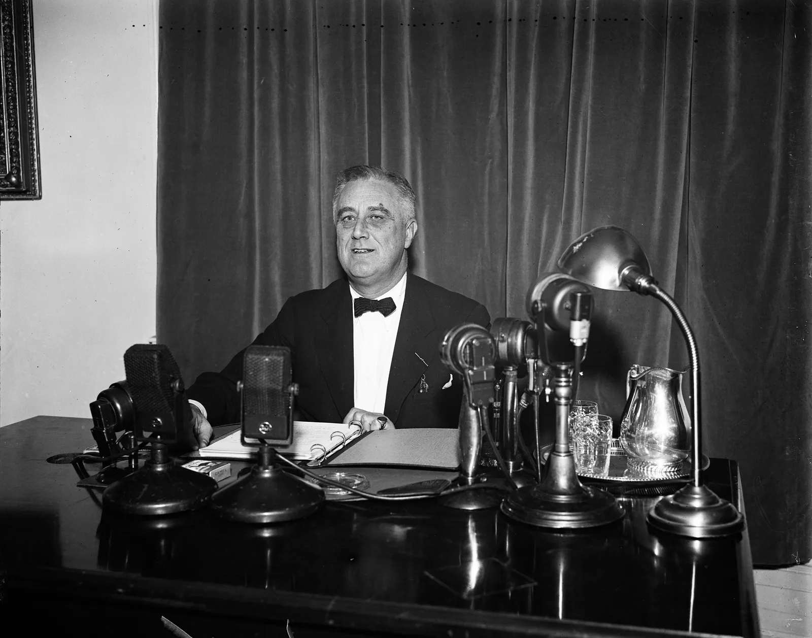 President Franklin D. Roosevelt seated at a desk crowded with radio network microphones during a 1937 fireside chat