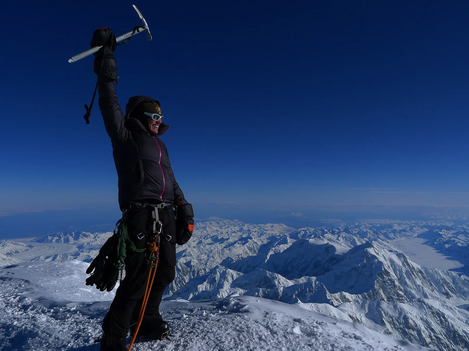 A mountaineer on a summit in the Alaska Range overlooking snow-covered peaks and glaciers