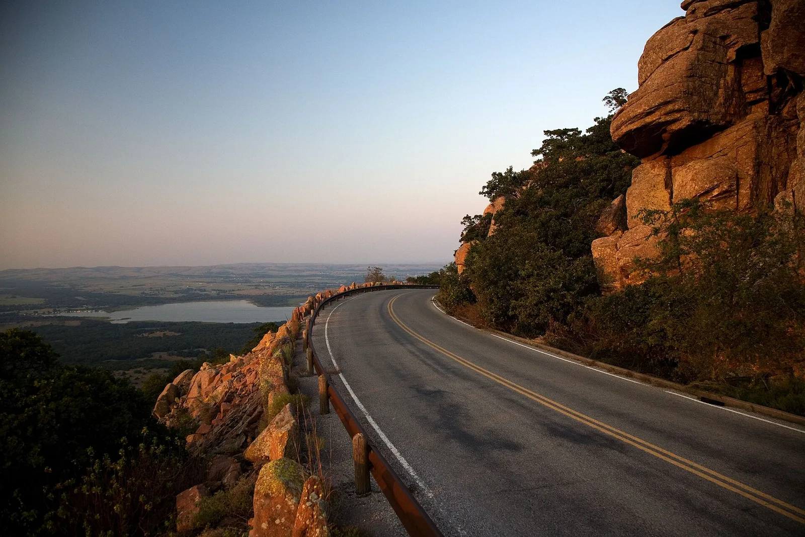 The road climbing Mount Scott past granite outcrops in the Wichita Mountains of Oklahoma, with a lake and the plains below